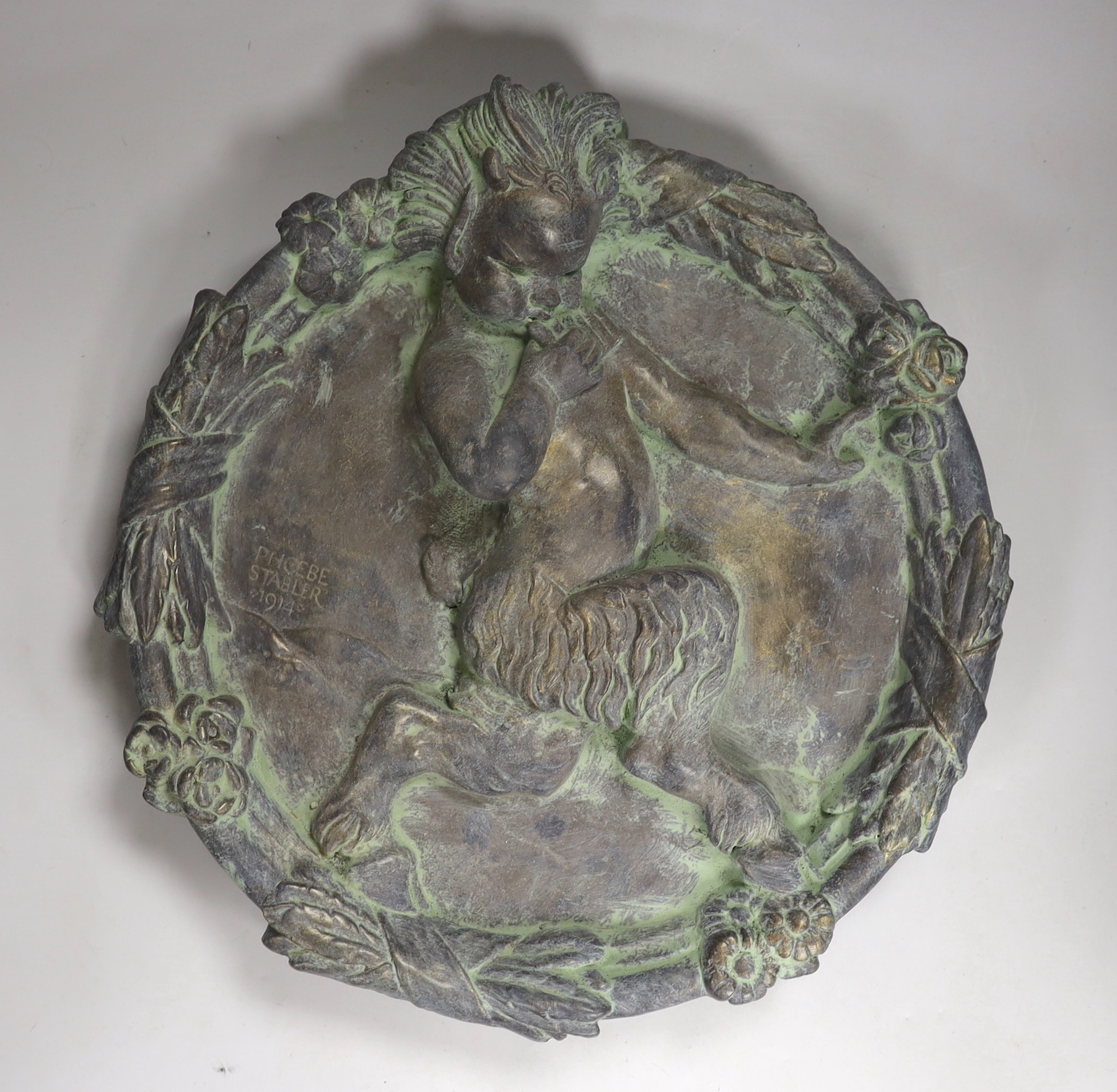 Phoebe Stabler (1879-1955). 'The Piping Faun', a patinated copper covered plaster roundel plaque, signed and dated 1914, cast in relief with a central faun framed by a decorative garland border, 44cm x 42cm